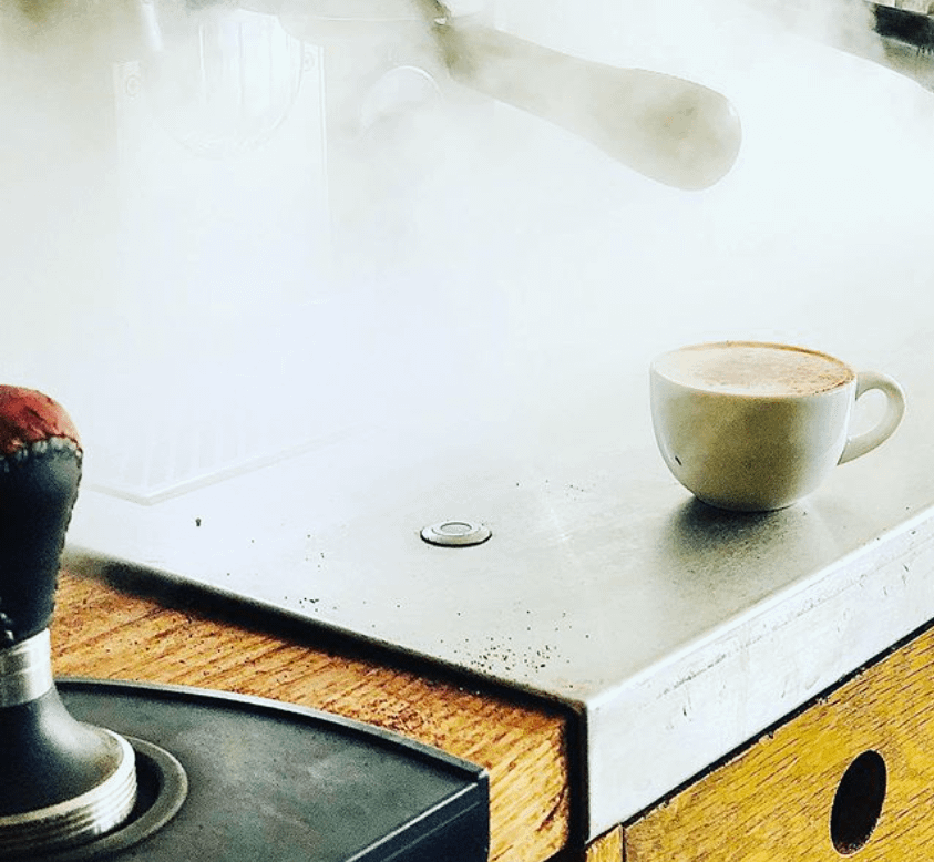 Steaming coffee machine with cappuccino on the side.